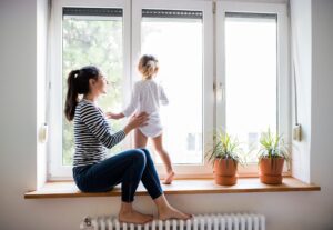 Mother and child sit on window sill and look out at backyard 