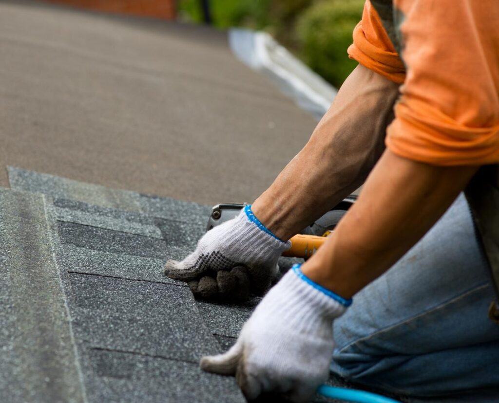 A roofing contractor presses a shingle down onto a roof.